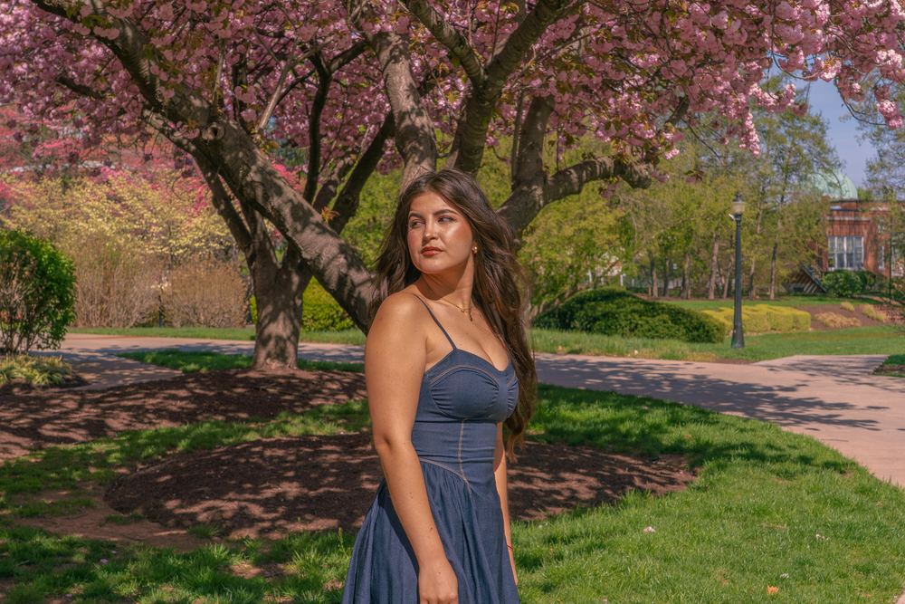 Woman in a blue dress standing beneath pink cherry blossoms