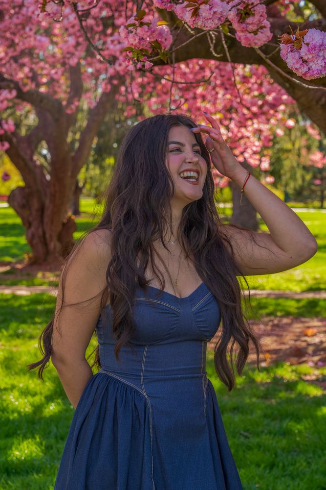 Woman in a blue dress laughing beneath pink cherry blossoms