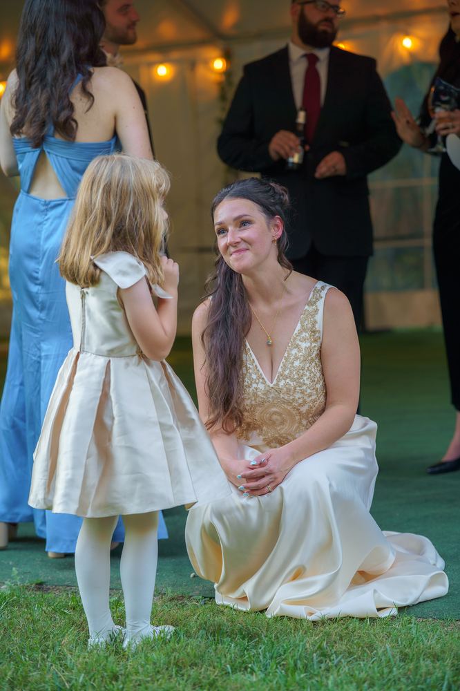 Person in a wedding dress kneeling beside a child in a light-colored dress