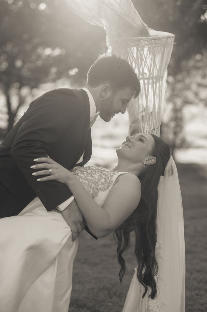 Black-and-white wedding photograph of a couple sharing a dip beneath a draped arbor